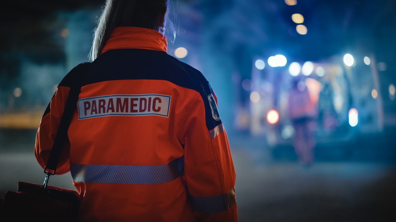 Secouriste de dos, de nuit, devant un véhicule d'urgence